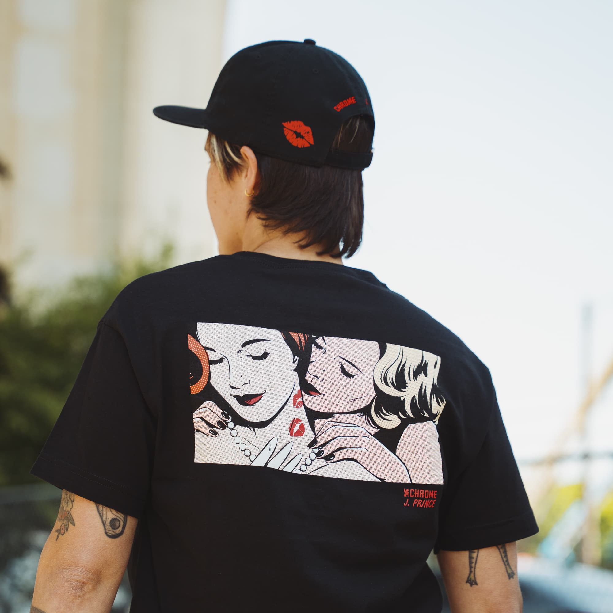 Person wearing a black t-shirt with graphic design on the back, standing outdoors.