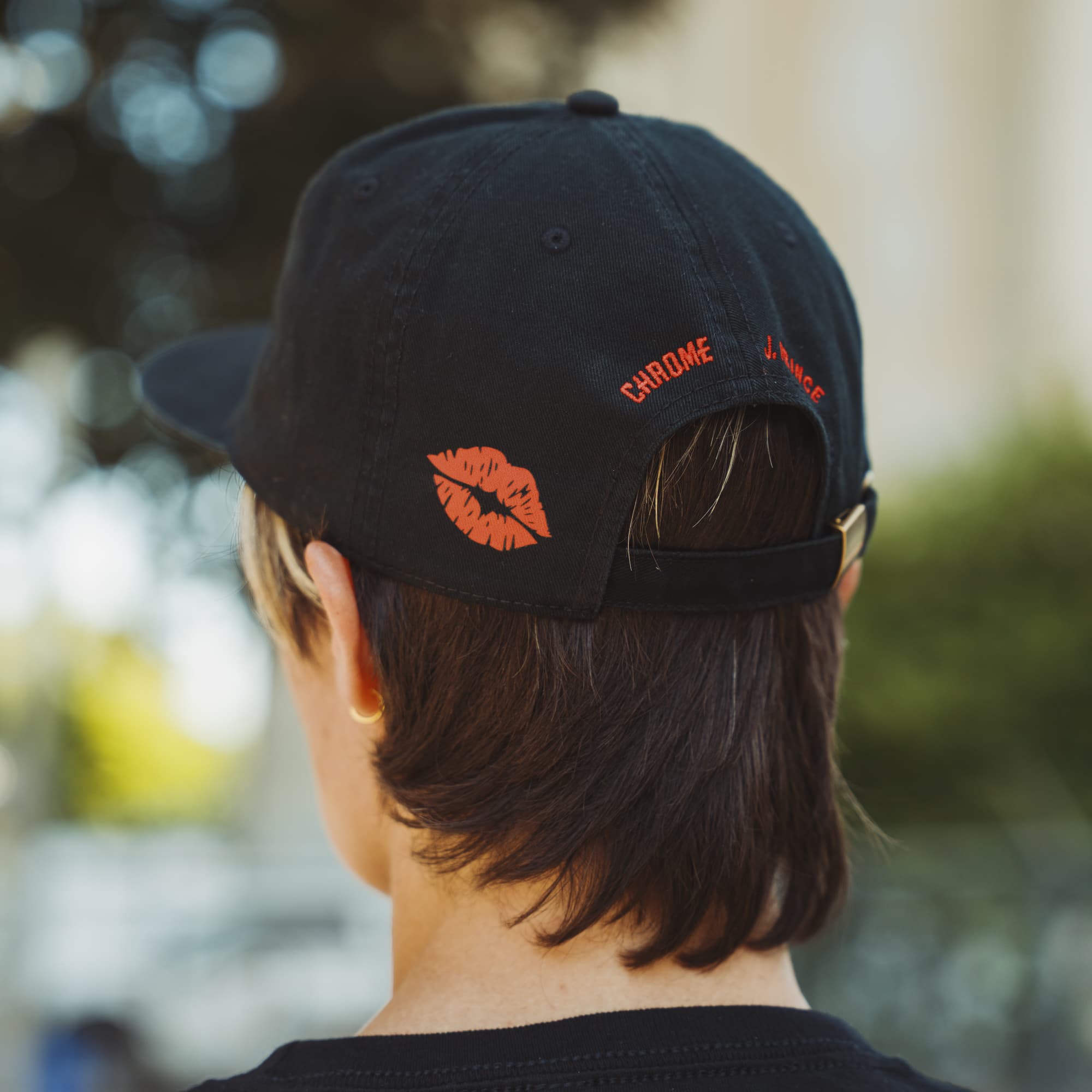 Person wearing a black cap with red text and logo, blurred outdoor background