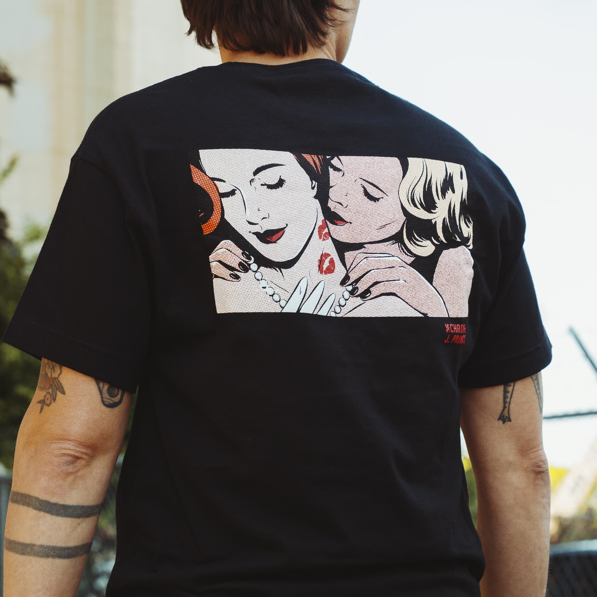 Person wearing a black t-shirt with a graphic design on the back, standing outdoors.